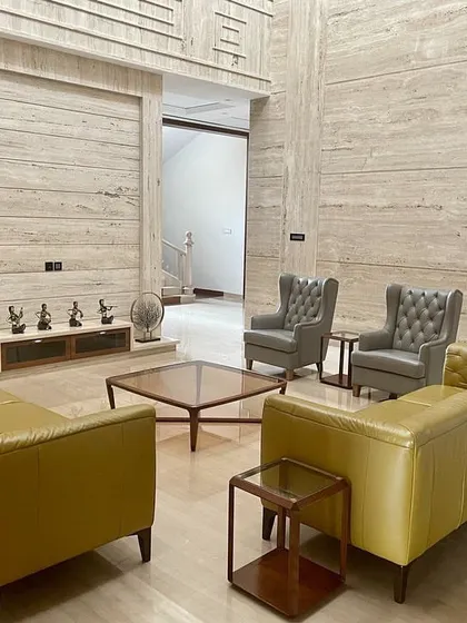 Another seating arrangement in the Tirupur residence, showcasing high-back chairs and minimalist sofas against a backdrop of full-height marble wall cladding.