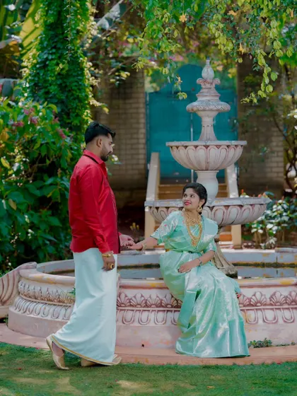 A romantic moment by a garden fountain. The bride's light green silk saree and the groom's red shirt and dhoti create a striking contrast.