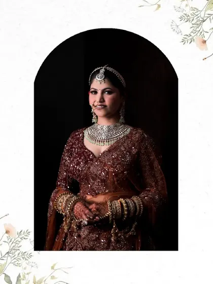 A classic bridal portrait in a maroon lehenga, framed within an arch, showcasing her complete look and heavy diamond necklace.
