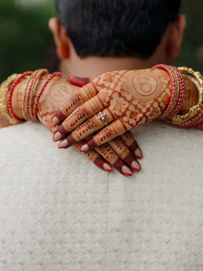 A close-up of the bride's hands, adorned with intricate henna and bangles, wrapped around her groom. This shot is all about the details and the connection they represent.