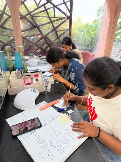 Close-up of a student meticulously working on a nail art design, with her notes by her side for reference.