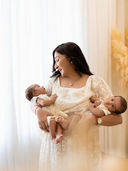 A mother's love, times two. This beautiful mother holds both of her newborn twins, looking from one to the other with a radiant smile. The soft lighting by the window adds a dreamy feel to this portrait.