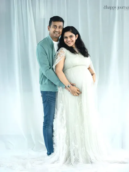 A classic and bright couple's portrait. The mother-to-be in a white lace gown and her partner create a timeless image of love and anticipation.
