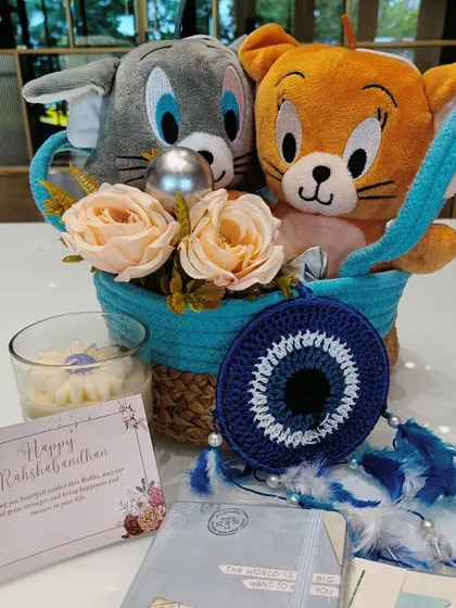 The complete Tom & Jerry Rakshabandhan hamper, including plushies, a dreamcatcher, a scented candle, and a personalized card, all arranged in a lovely blue basket.