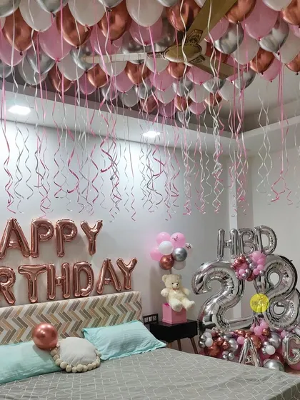 A classic birthday room decoration. We filled the ceiling with pink, rose gold, and silver balloons with dangling ribbons and set up large foil number balloons to create a festive and surprising atmosphere.