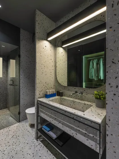 A view of the master bathroom in 'A Hint of Azul', showing the custom terrazzo vanity and integrated sink. The reflection in the mirror reveals the adjoining walk-in closet, highlighting the fluid connection between spaces.