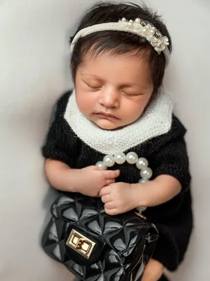 The final portrait from our little fashionista session. The baby is dressed in a classic black-and-white knit outfit, holding a string of pearls and a tiny handbag.