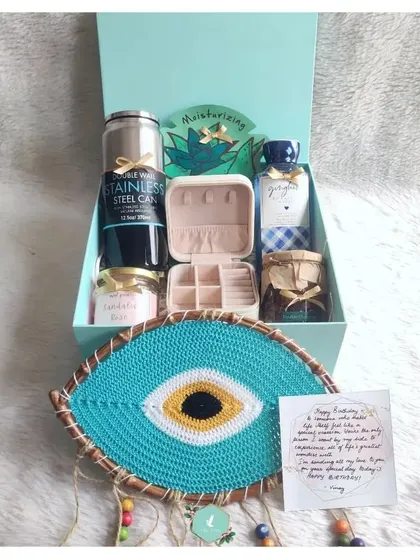 This birthday hamper is designed to bring calm and positive vibes. It features a beautiful handmade evil eye dreamcatcher, a jewelry box, a scented candle, and a stainless steel can for her favorite beverage.