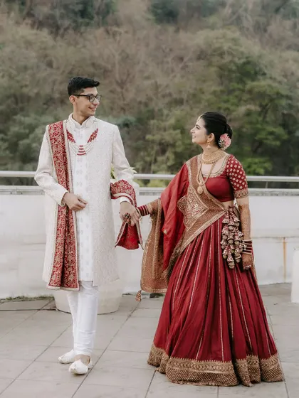 The bride and groom walk hand-in-hand. This portrait showcases their coordinated red and white outfits and the easy elegance of their connection.