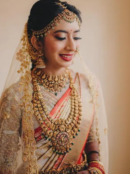 This bride looks ethereal with a delicate veil over her head. Her custom off-white and gold ensemble is perfect for a traditional yet modern wedding.
