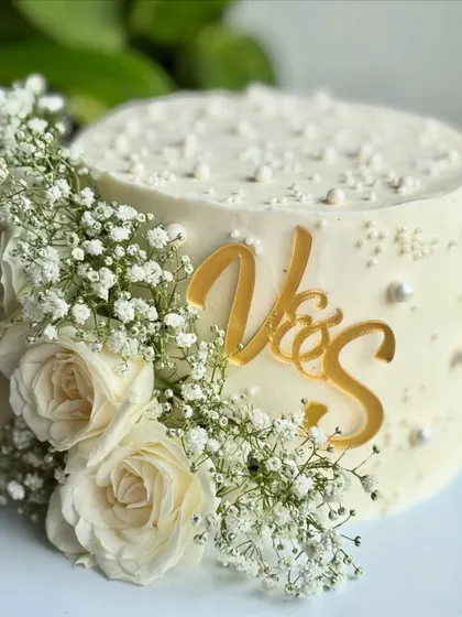 This angle showcases the depth of the floral arrangement and the shimmer of the gold topper against the pristine white buttercream.