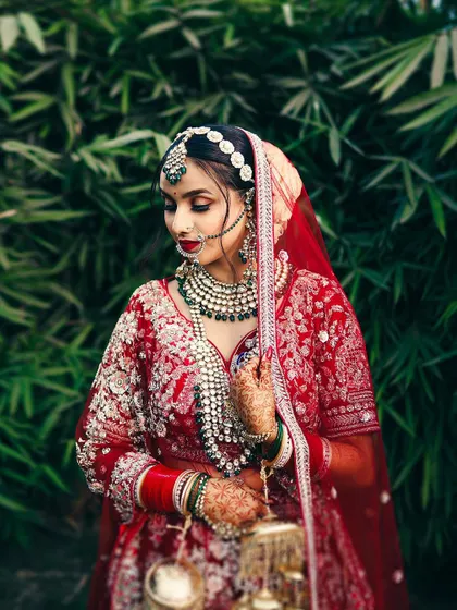 A detailed portrait of a bride in her red lehenga, set against a rich green backdrop. We focus on the intricate details of her jewelry, makeup, and the delicate kalire.