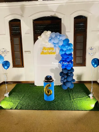 A simple and stylish 6th birthday setup. This outdoor decoration features a white arch backdrop with a blue ombre balloon garland and a plinth for the cake, creating a clean and modern look.