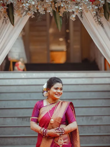 The bride's happy smile as she stands under a floral archway. This portrait is full of light and joy, perfectly capturing the wedding day atmosphere.