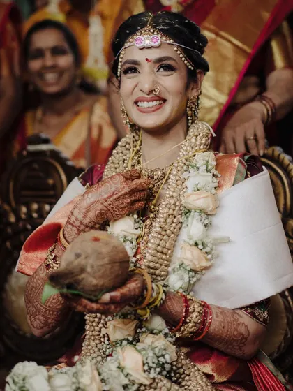 This South Indian bride, holding a coconut, is the picture of ceremonial grace and happiness. The warm lighting and her genuine smile make this a beautiful, candid capture of a key wedding moment.