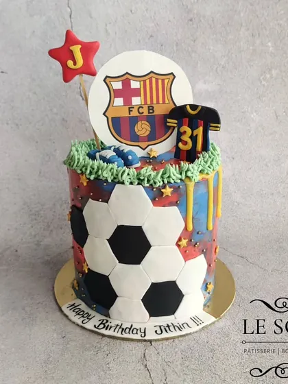A vibrant football-themed cake for a FC Barcelona fan. This 1 kg Pineapple cake is designed to look like a soccer ball and is topped with the team's logo and a jersey.