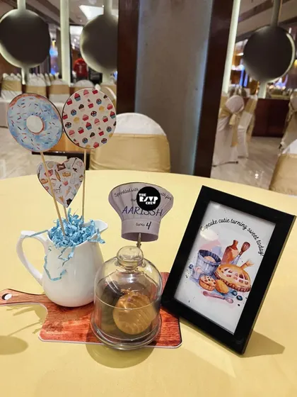 A sweet baking-themed centerpiece with donut and cupcake cutouts, a mini chef's hat, and a framed illustration.
