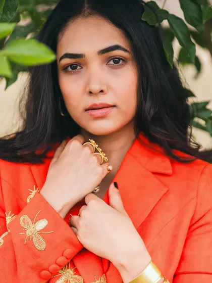 A close-up portrait of the client, framed by leaves, in her custom orange suit.