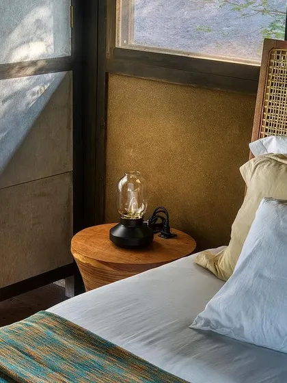 A close-up of the bedside in the earthen studio. The play of natural light on the textured walls and simple, elegant furnishings creates a serene and restful atmosphere.