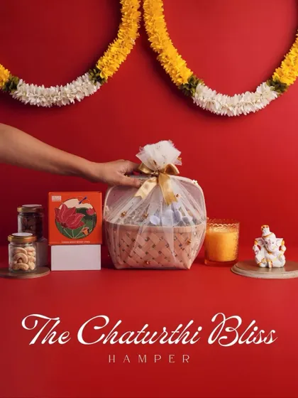 "The Chaturthi Bliss Hamper" is a perfect offering for Ganesh Chaturthi. This beautifully arranged gift includes a Ganesha idol, a candle, and jars of cashews and almonds.
