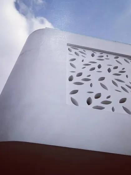 A close-up, upward-angle shot of the perforated wall detail. This perspective emphasizes the clean, curved form of the building against the sky and the intricate pattern of the screen.