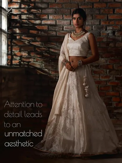 Attention to detail leads to an unmatched aesthetic. This full view of a white and gold lehenga highlights the intricate brocade work and the graceful fall of the fabric.