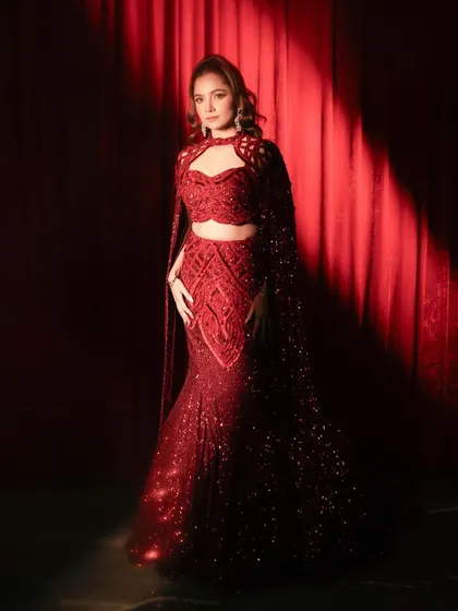 A client shines in a ruby red embellished lehenga with floor-sweeping sleeves and signature cutwork embroidery, a silhouette that moves with grace.