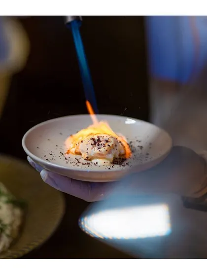 We love creating exotic and theatrical food experiences. Here, a dish is being finished with a blowtorch, adding a touch of fire and drama right at the table.
