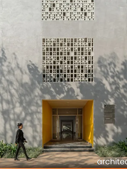 The entrance to Vidyashilp Academy, a UNESCO Happy School, is marked by a bright yellow portal set within a facade of concrete and 'jaali' screens. The design is functional and eco-conscious, creating an enriching experience for students.