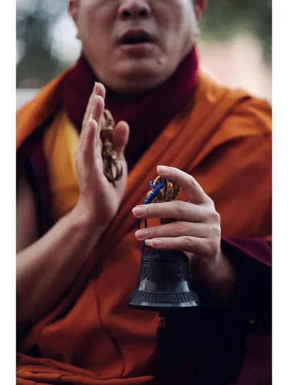 A close-up shot focuses on the hands of a monk holding a vajra and ghanta (bell) during a chant. This detail-oriented photo highlights the specific ritual objects and gestures central to Buddhist practice.