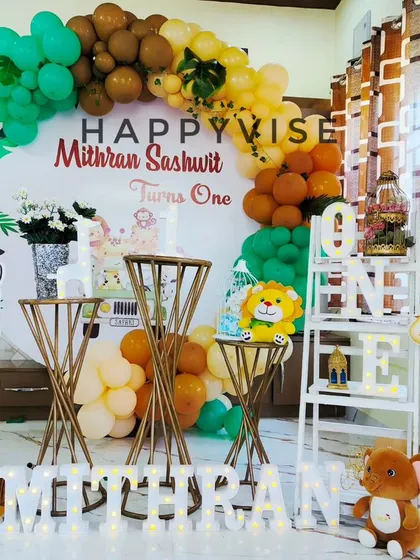 A bright and cheerful safari theme for Mithran Sashwit's first birthday. The setup includes large zebra and giraffe cutouts, plush animals, and a balloon arch in jungle-inspired colors.