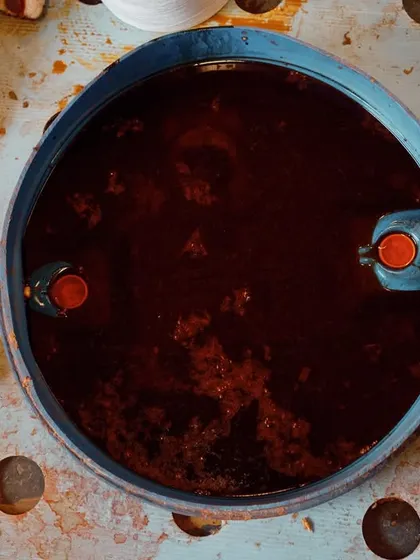 This is where color comes to life. An abstract, top-down shot of a dye vat, capturing the deep, rich hue and the raw, industrial start of a color story for a textile brand.