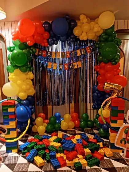 A fun and interactive Lego-themed birthday party. The decoration includes columns made of Lego-like blocks, a colorful balloon arch, and a pile of large blocks for kids to play with.