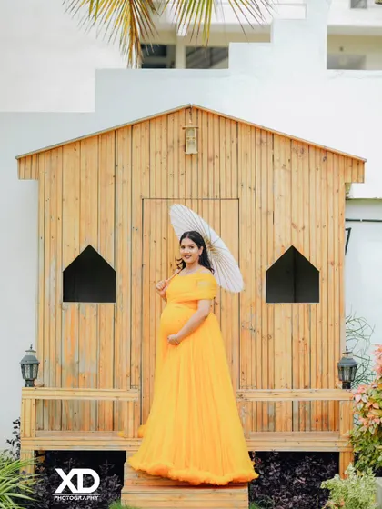 A beautiful solo portrait of the mother-to-be in a yellow gown, holding a paper umbrella in a rustic setting.