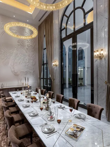 The dining room of The Grand Alabaster, a space designed for lavish entertaining. Double-height arched windows, a massive crystal chandelier, and a custom relief wall sculpture create an atmosphere of unparalleled luxury.