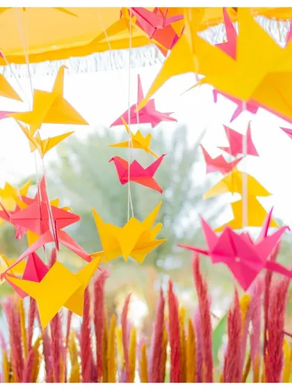 Pink and yellow origami birds hang from the ceiling at a Mehendi ceremony. This unique and playful decor detail added a touch of whimsy and color to the event.