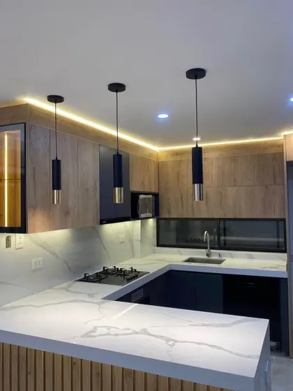 This kitchen features a stunning combination of wood, marble, and dark blue cabinets. The pendant lights and under-cabinet lighting work together to create a warm and well-lit environment.