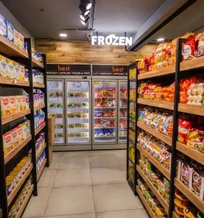 The frozen food section, clearly marked with illuminated signage. We integrated the refrigeration units seamlessly into the wooden shelving for a clean, organized look.