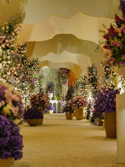 A view down the floral-lined pathway, with its undulating, cave-like ceiling. The path is lit by the soft glow of the flowers and hidden lights, creating a magical journey for guests.