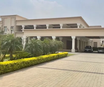 The grand driveway approach to the Tirupur residence, lined with lush hedges and palm trees, leading to the impressive marble-clad facade and columned veranda.