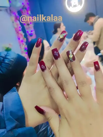 A deep, glossy maroon polish on square-shaped nails. This set is enhanced with a single accent nail featuring an intricate gold and crystal design, showing how to elevate a classic manicure.