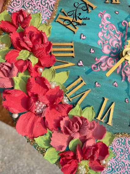 A close-up of a warm-toned wall clock, featuring deep red sculpted flowers against a teal and pink background. The pearl accents add a touch of elegance.