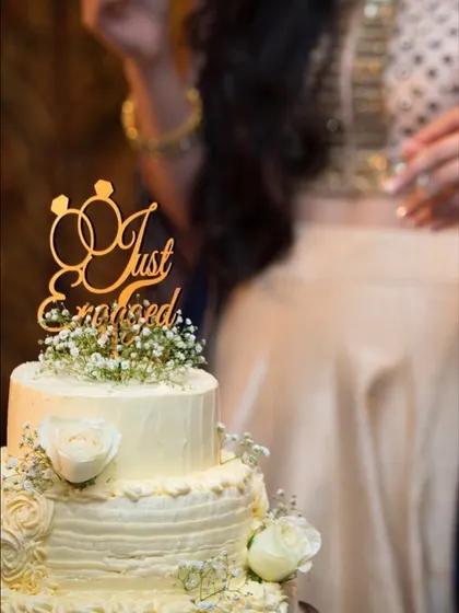 A classic two-tiered cake for a "Just Engaged" celebration, adorned with delicate baby's breath and fresh white roses. This elegant design is perfect for engagement parties, anniversaries, or intimate weddings.