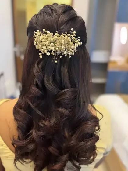 A half-up style with defined curls, featuring a large, elegant accessory made of dried baby's breath.