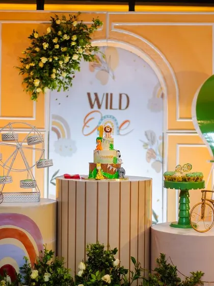The cake takes center stage in this beautiful boho setup. The backdrop features a 'Wild One' sign, a hot air balloon, and friendly animal characters, all tied together with soft, natural colors.