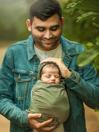 A father gently holds his swaddled newborn, looking down with a soft, loving expression. This close-up portrait beautifully captures the quiet, powerful bond between a father and his new baby.
