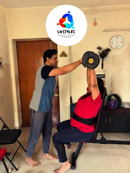I am assisting a client with a seated overhead dumbbell press, helping her maintain stability and proper form to strengthen her shoulders.