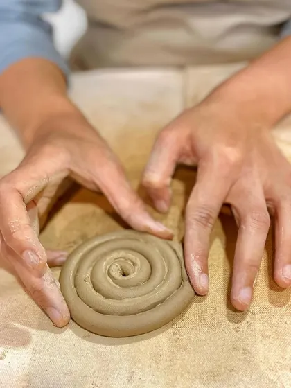 The coiling technique involves rolling out long ropes of clay and building them up, layer by layer. Here, a student is starting the base for a coiled pot.