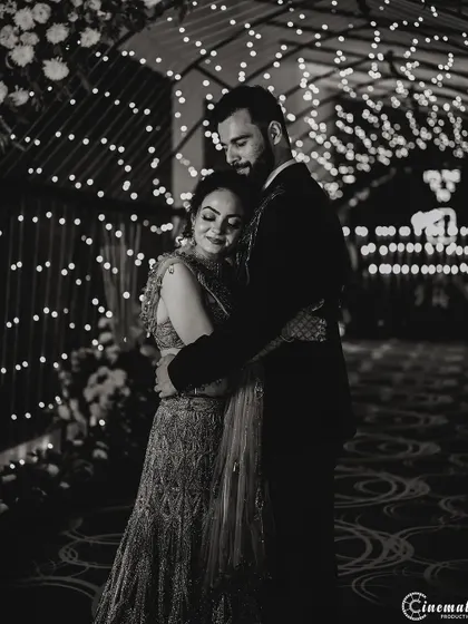A romantic black and white photo of the couple sharing a quiet moment amidst the celebration. The fairy lights create a beautiful bokeh effect, adding to the magical feel.