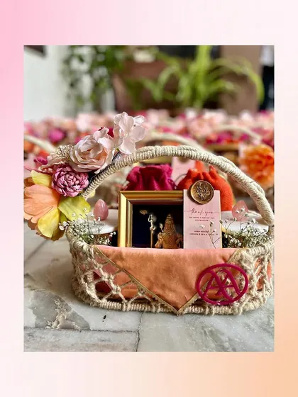 A single handcrafted favor basket, showcasing the personalized monogram, a framed deity, and a wax-sealed thank you note. The floral arrangement on the handle adds a final touch of beauty.